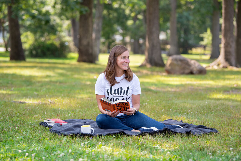 A female coach is sitting at a park on a blanket with her favorite books.