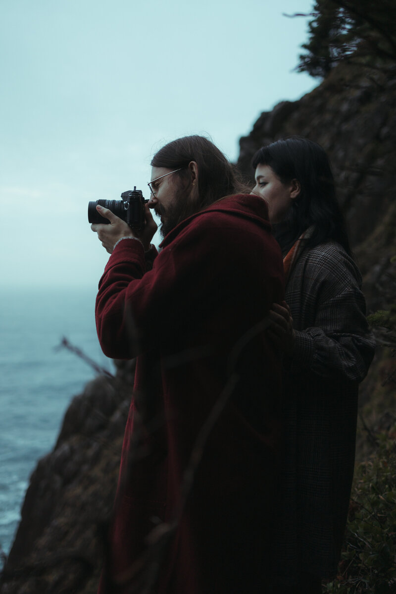 Micro Wedding photographers Kelsey and Michael Bandhauer of Semperflora look over the edge of Elk Flats on the Oregon Coast and take a photo through a vintage film camera.
