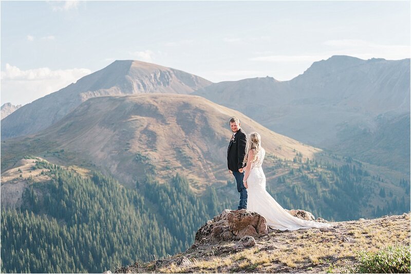 A couple stands on the side of a mountain pass at sunset in Colorado