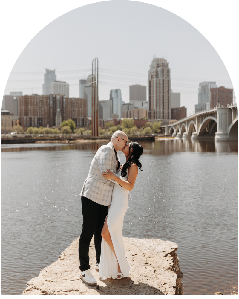 Bride and groom standing on rock with Minneapolis skyline behind them and kissing each other