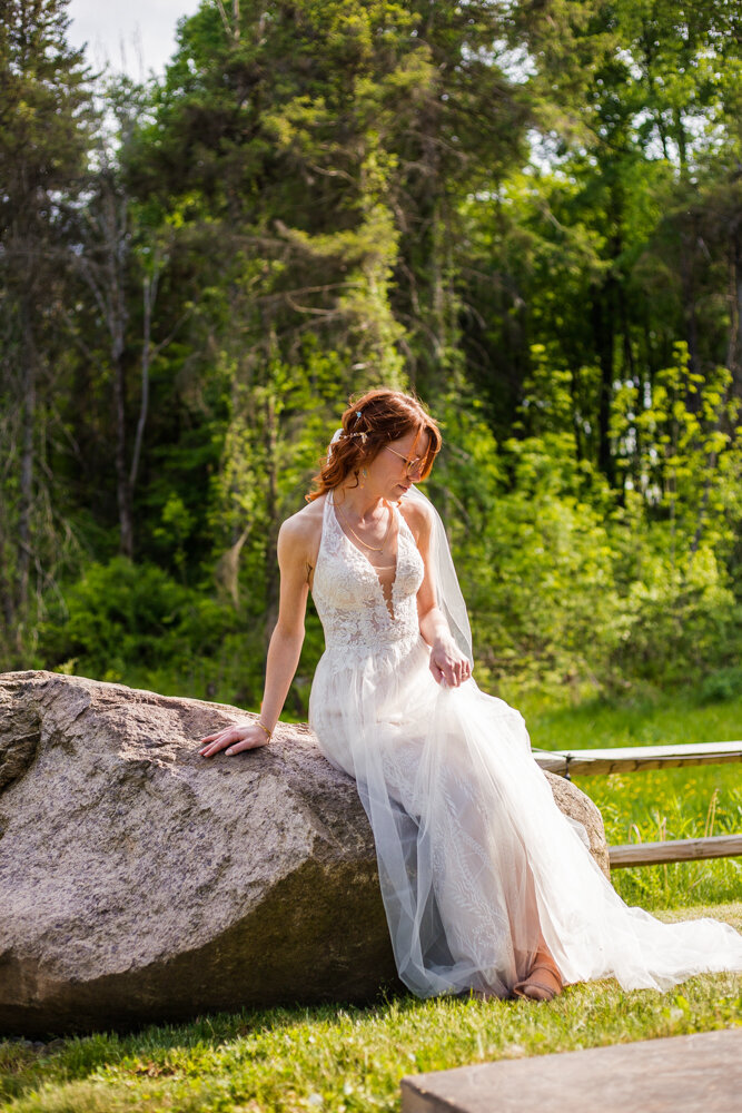 Bride sits alone on a large boulder located at Pine Junction in Sherman, NY