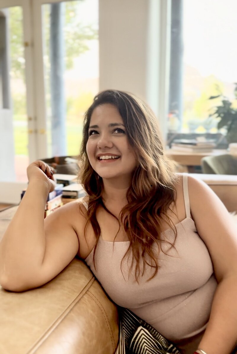 Women in golden light, wearing dark rimmed glasses and striped shirt, smiling down at her hands as she rolls out clay