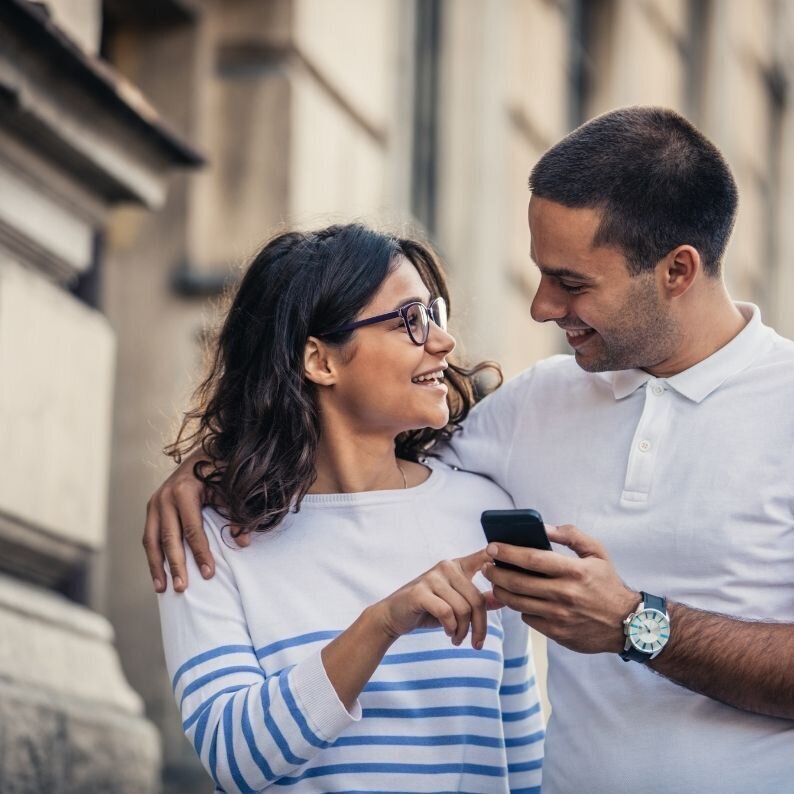 A woman points to something on her partners phone as the two smile. This could represent a couple taking the first steps towards a couples therapy program in Florida. Contact a couples therapist in Florida for support in nurturing your relationship.
