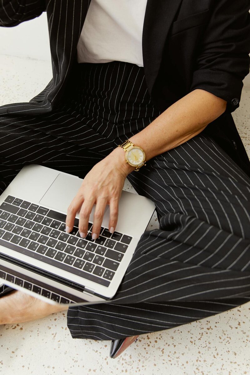 woman in a pinstripe suit and gold watch on her laptop