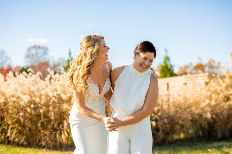 Two brides with their arms around each other leaning over and laughing.