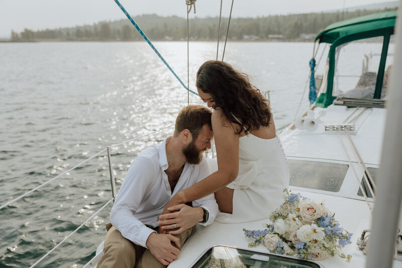 bride and groom on a sailboat on the north shore of minnesota. couple is laughing and leaning into eachother. photo by a Minnesota Elopement Photographer