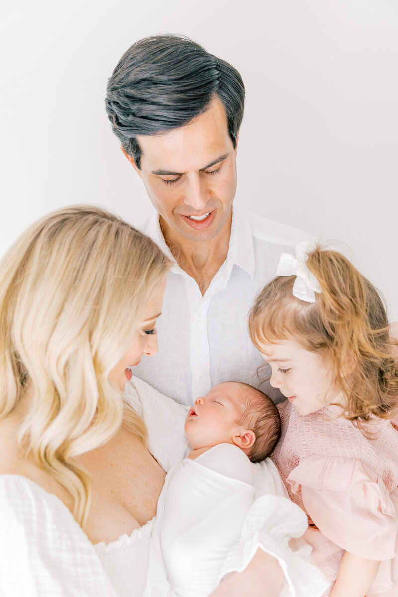 A mom and dad hold their sleeping newborn baby and toddler daughter while standing in the studio of a Charlotte Family Photographer