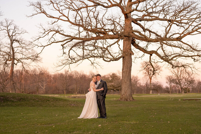 Couple smiles under a large tree at sunset