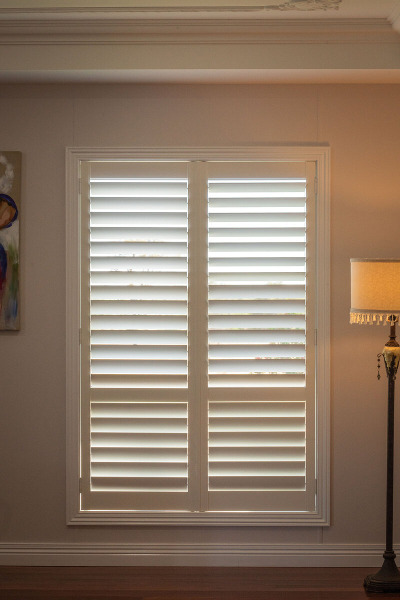 Interior window featuring custom white hinged shutters, providing privacy, light control, and energy efficiency.