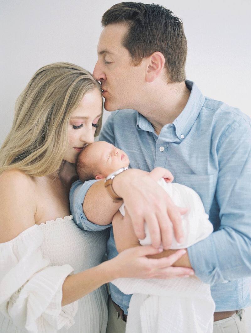 Father kisses his wife on the head while they hold their newborn photographed by DC Newborn Photographer Marie Elizabeth Photography