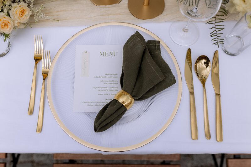 Detailfoto von Tischgedeck mit goldenem Besteck und schwarzer Serviette