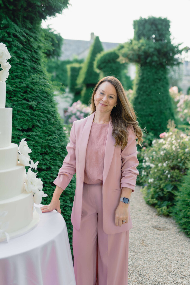 luxury event planner emma westacott poses next to a wedding cake in the gardens of euridge manor