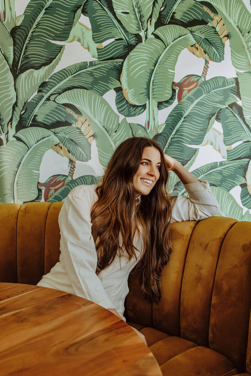 woman sitting at a table in front of palm leaf wallpaper