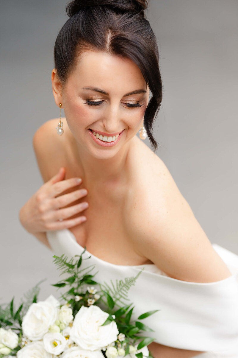 Ottawa wedding photography of a bride in an off-the-shoulder dress looking down at her bouquet and laughing.  Taken  outdoors at the Chateau Laurier by JEMMAN Photography