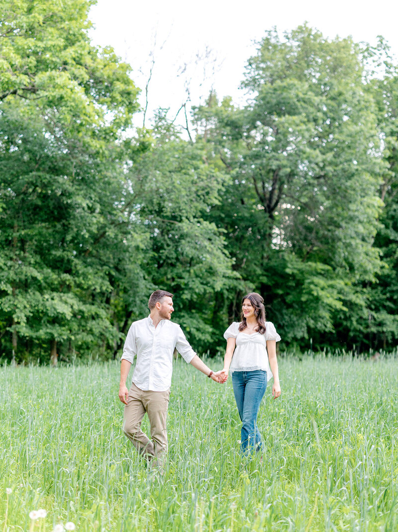 Couple holding hands and walking through a grassy field
