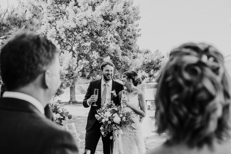 Bride and groom are wrapped in an embrace with their heads touching for a wedding day portrait photo. Behind them are grape vines at a Niagara, ON winery. Captured by top Niagara wedding photographer Ashlee Ellison.