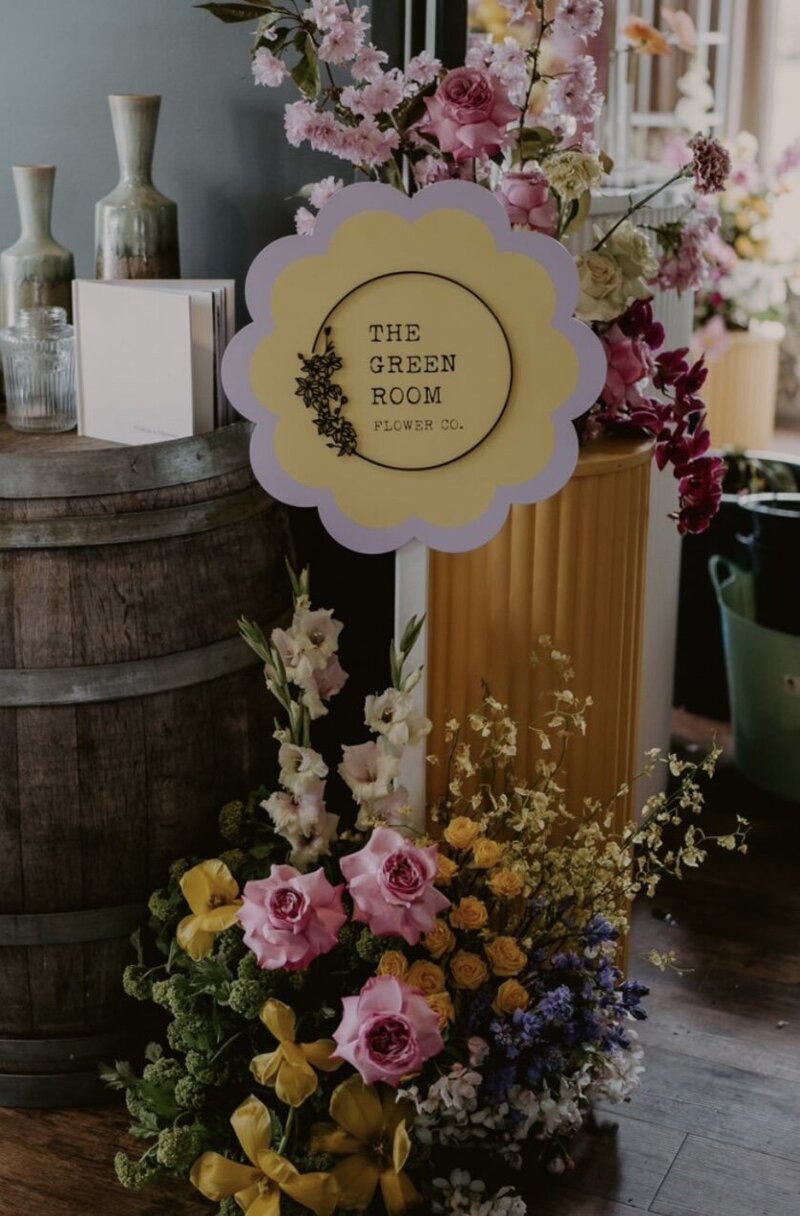 a beautiful soft yellow and lavender wavy sign on a post with lovely pastel florals showcasing the sign
