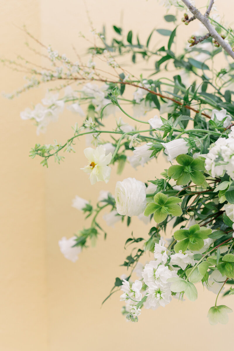 White and green wedding reception bar flowers with yellow wall.