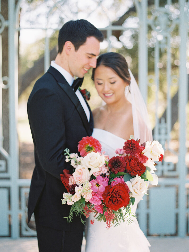 Classic wedding portrait with a striking bouquet of red, blush, and white flowers—elegant with a bold twist.