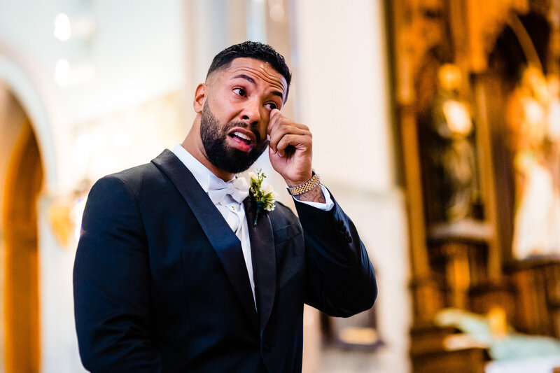 A groom wiping a tear from his face as the bride walks down the aisle at the Historic St. Patrick's Cathedral  in Toledo Ohio