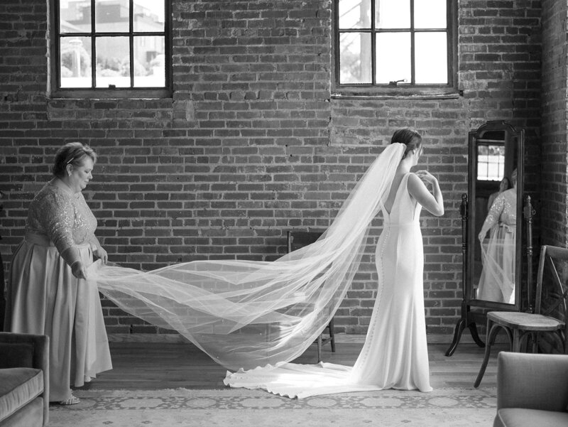 A bride's mother adjusts her veil while she looks into a mirror