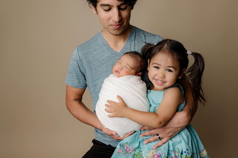 dad holds his newborn baby boy and his toddler daughter during their studio newborn session