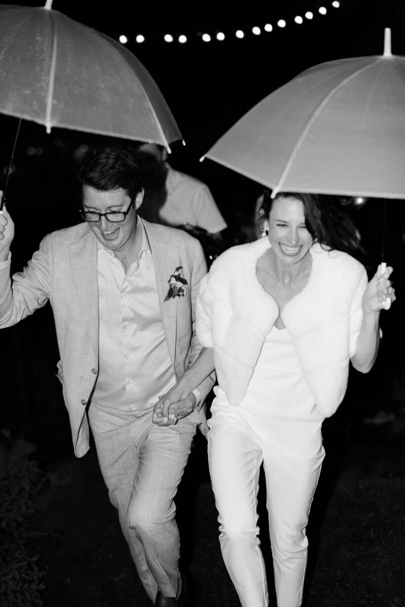 Newlyweds hold umbrellas as they leave their reception after dark in the Catskills