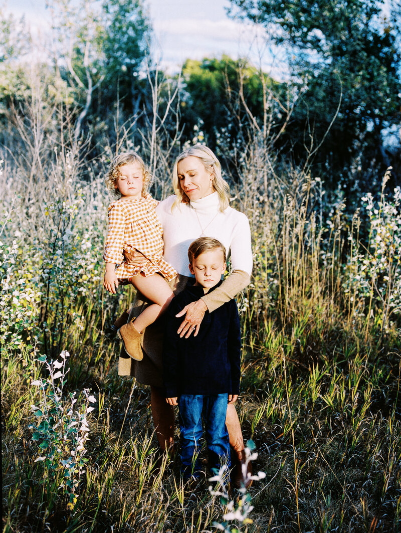portrait of mom and two kids standing  with eyes closed in tall grass