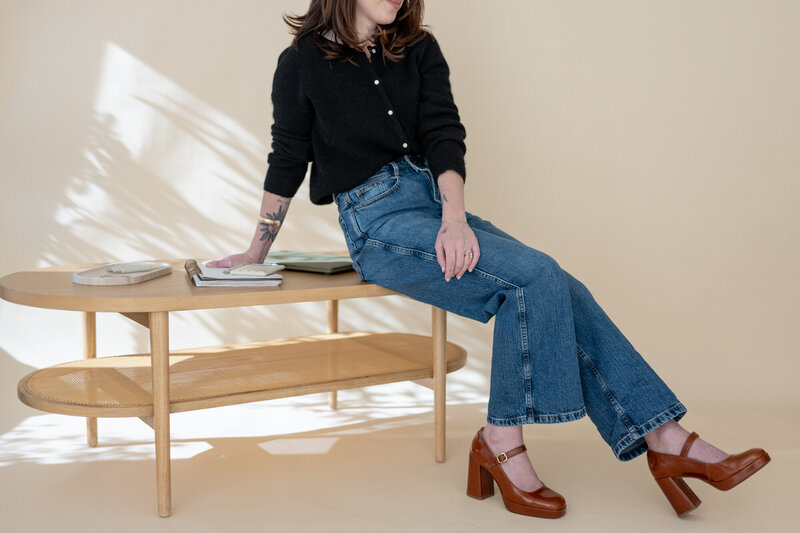 A branding photo of a educator sitting on a table with light shadows reflecting on the backdrop. 