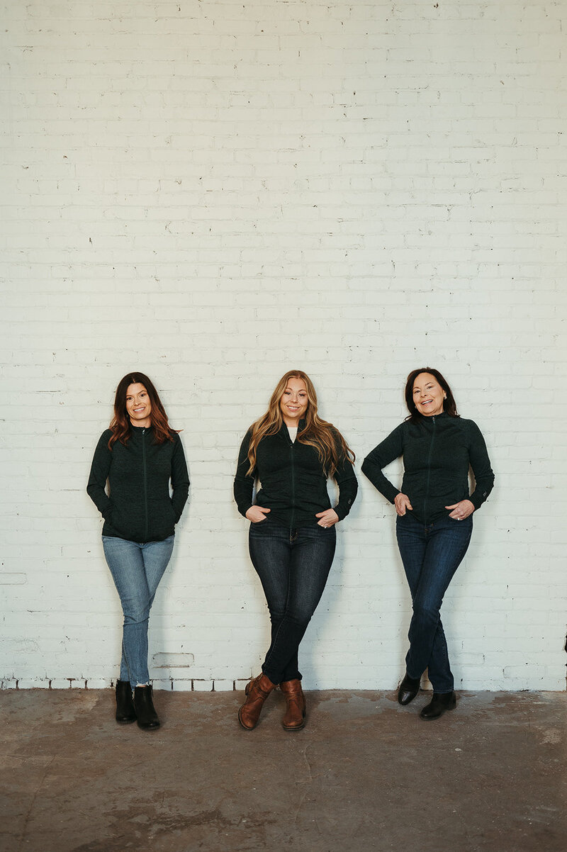 The Kalispell Denture studio team, Kelly, Beverly, and Katy smile at the camera while wearing black sweaters.