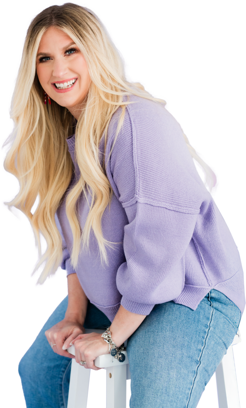Headshot of Brittany Kues, podcast growth coach and owner of Kues media, sitting on a stool. She is smiling directly at the camera. She is wearing a slouchy purple pullover and jeans with long blonde hair. 