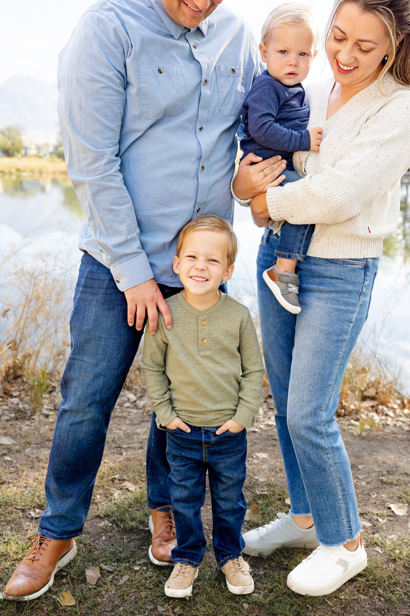 Cute young boy smiels right at the camera amidst his family smiling right at him.