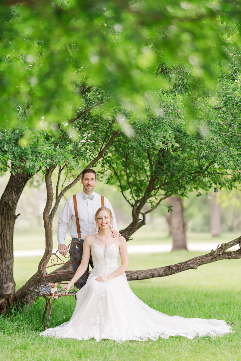 Bride-sitting-on-bench-groom-standing-portrait