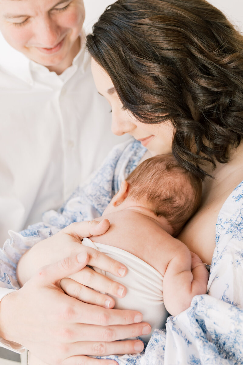 A mother cradles her sleeping newborn baby against her chest while sitting on a couch