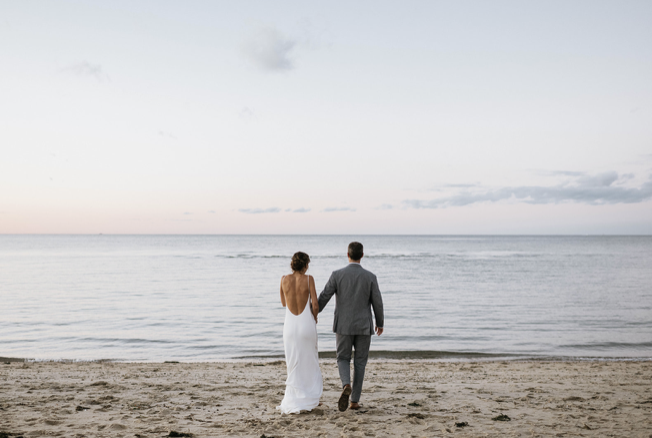 A man and woman holding hands walking on the beach towards the ocean on their wedding day