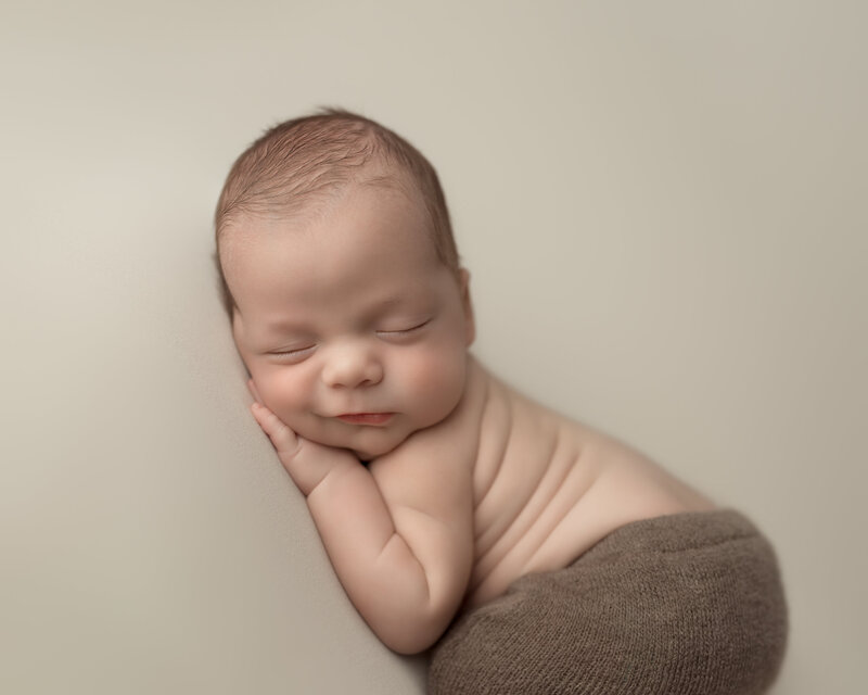 Newborn boy with a slight smirk in cozy brown tones – timeless side pose portrait in Paris, Ontario