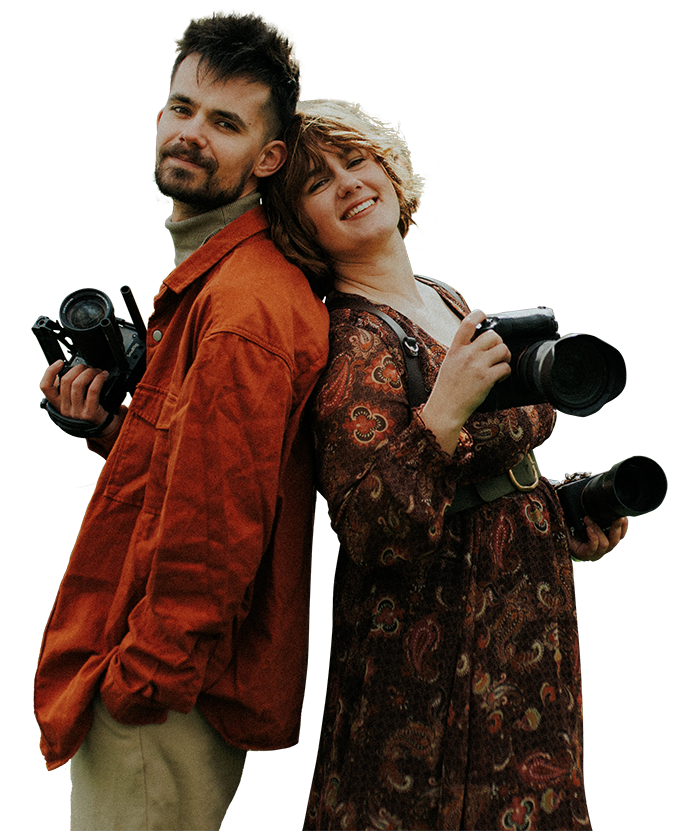 Léa et Nolan, photographe et vidéaste en bretagne, dos à dos, souriants, avec leurs appareils à la main. Photo détourée.