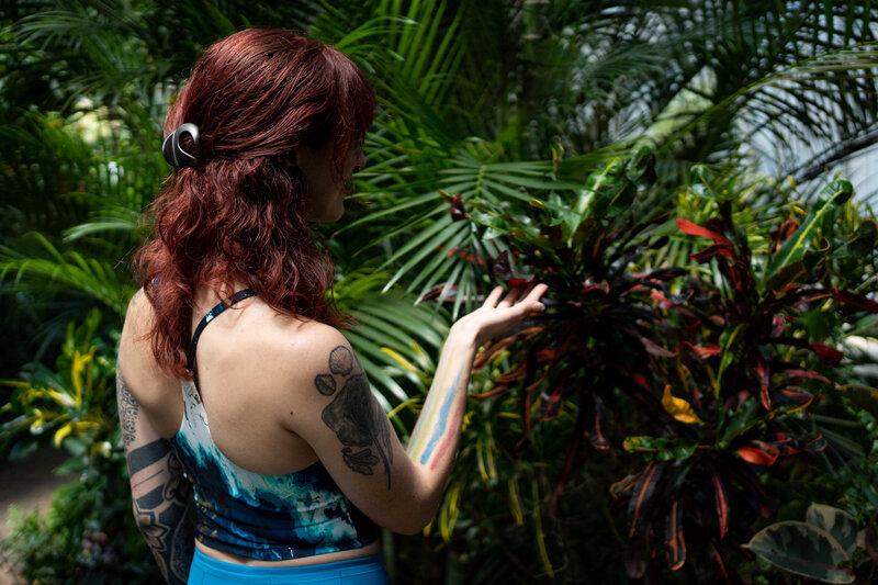woman with dark reddish hair puts her hand out towards a plant