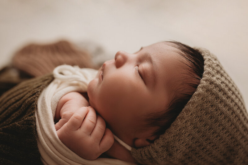Newborn baby boy photo shoot by Atlanta, Georgia newborn photographer  with baby boy in gray hat clasping hands under chin while sleeping.