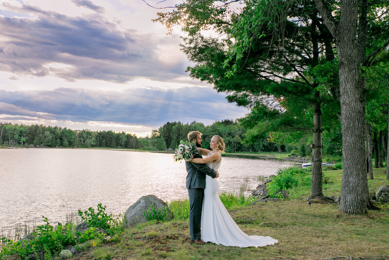 Bride and Groom with arms around each other standing by lake | Wedding Photography taken at Klein Wedding at Grace on the Lake in Maine
