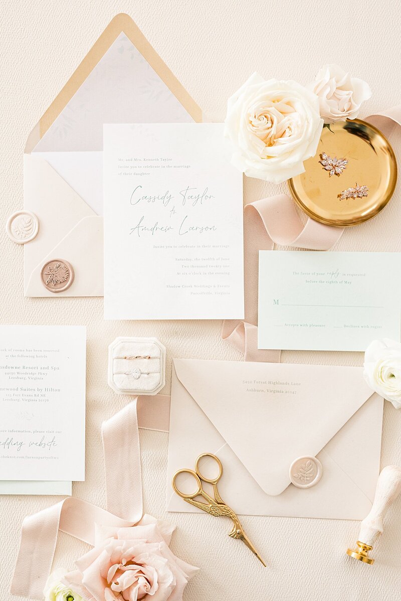 ivory and pastel pink wedding invitation suite  styled with gold accent accessories and matching wax seal.