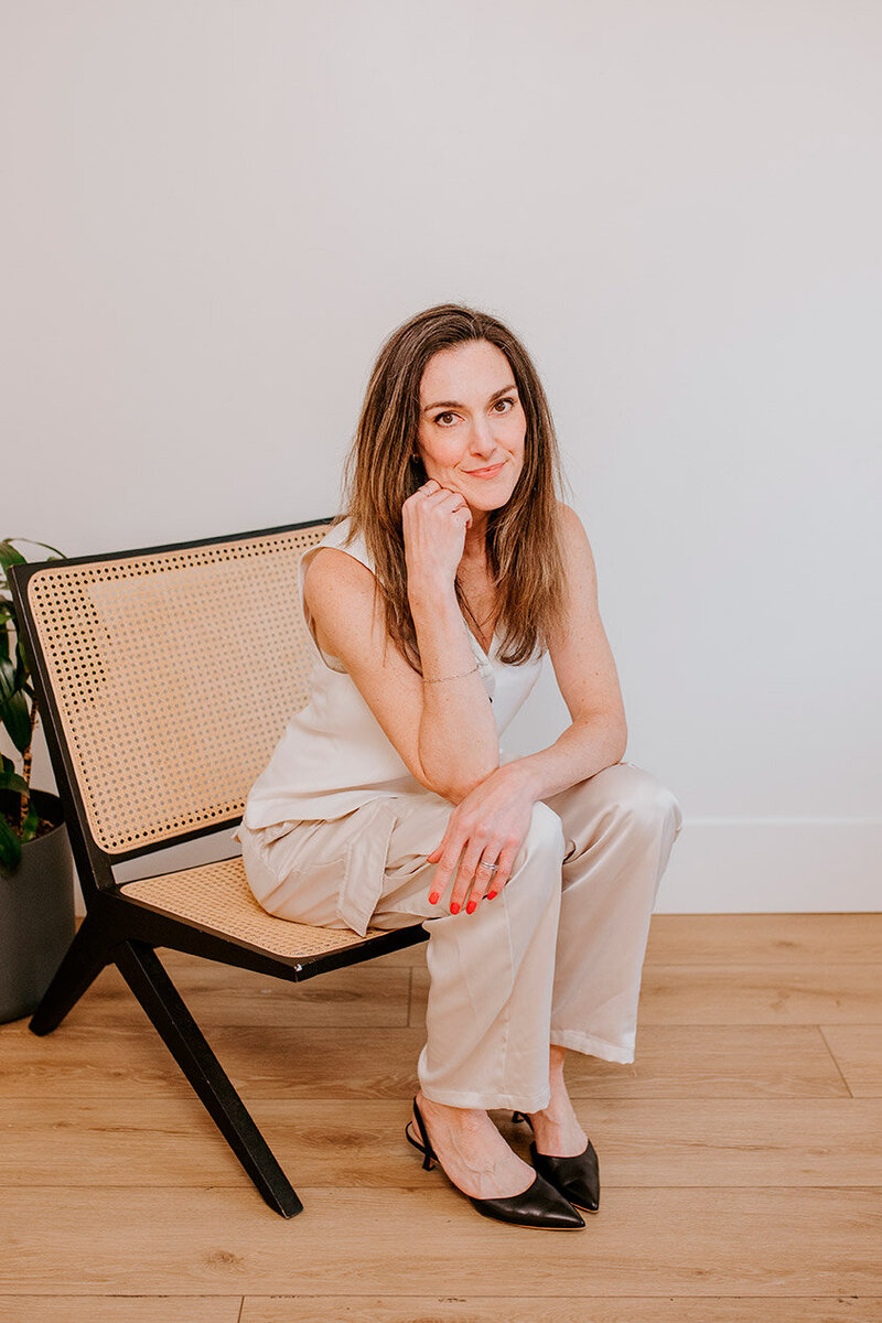 Laura Baer, founder of Baer Brand Studio, brand designer in Chilliwack British Columbia, sitting in a modern chair with a relaxed, professional pose, wearing neutral tones and black heels.