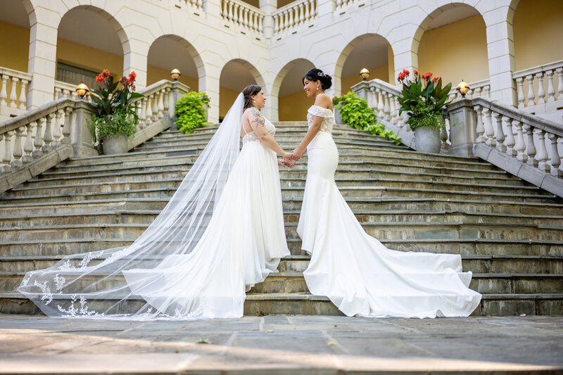 two brides facing one another holding hands outside of a villa at airlie on stone steps