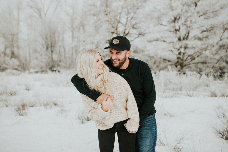 A couple hold one another playfully as they smile at one another in the snow