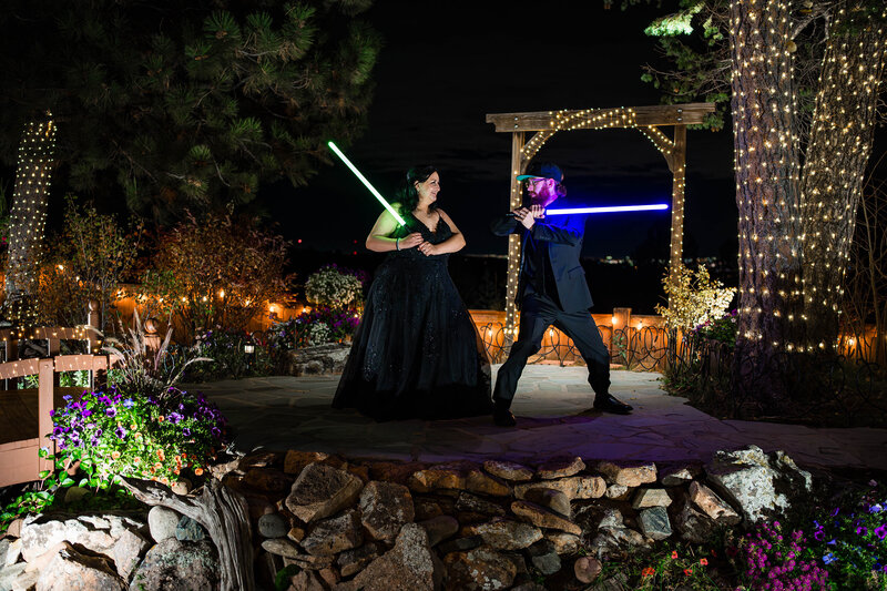 Star Wars Wedding theme and Bride and groom posing with glowing lightsabers during a dramatic night portrait at Christies of Genesee in Colorado.