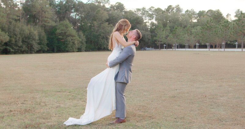 groom in gray suit holding bride in large open field, staring into each other's eyes at havana springs
