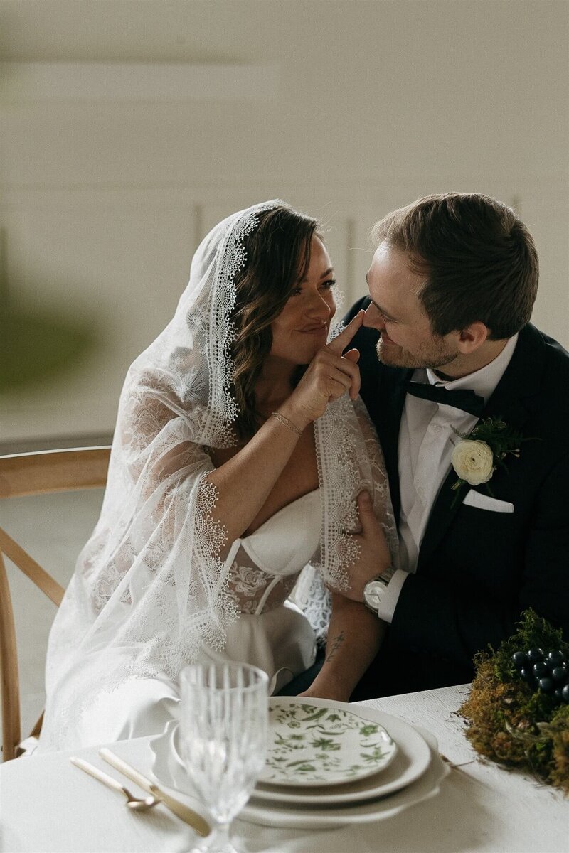 Bride taps groom on the nose in playful gesture while at their wedding reception.