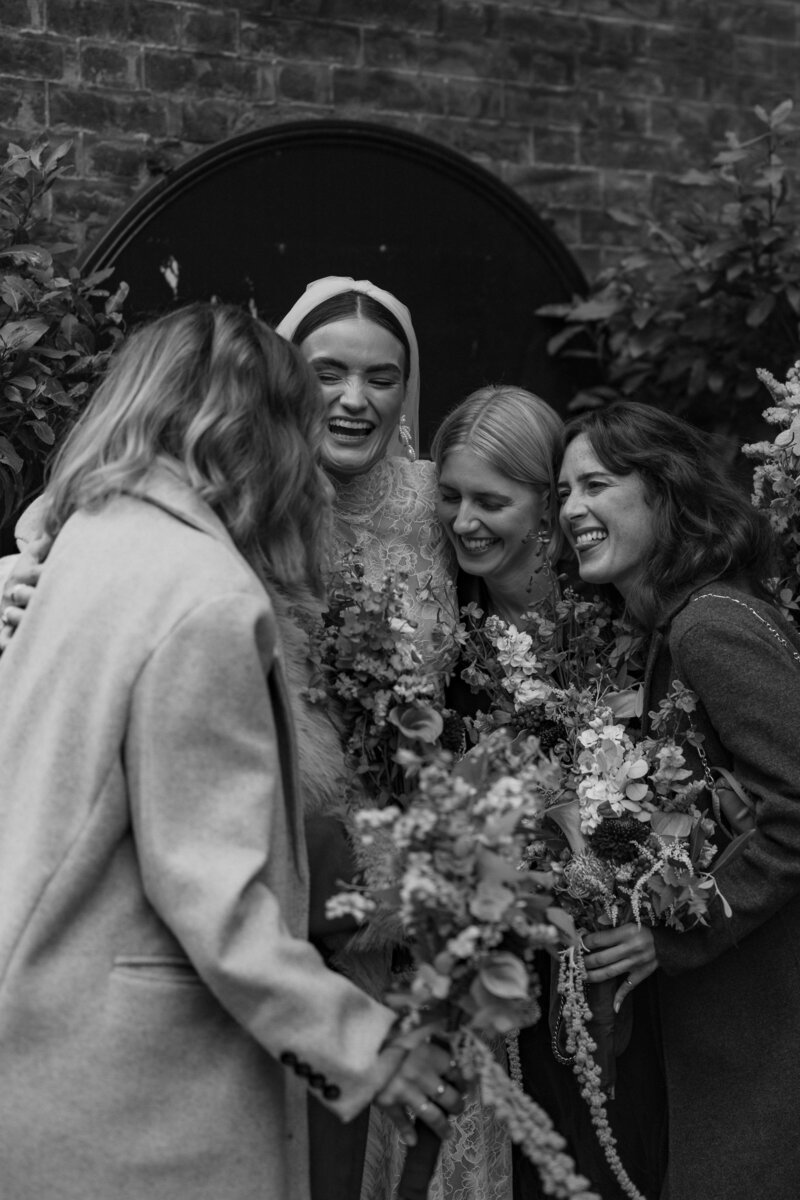 Bride and bridesmaids have a group hug outside the brides central london wedding venue st etheldreda's chuch farringdon