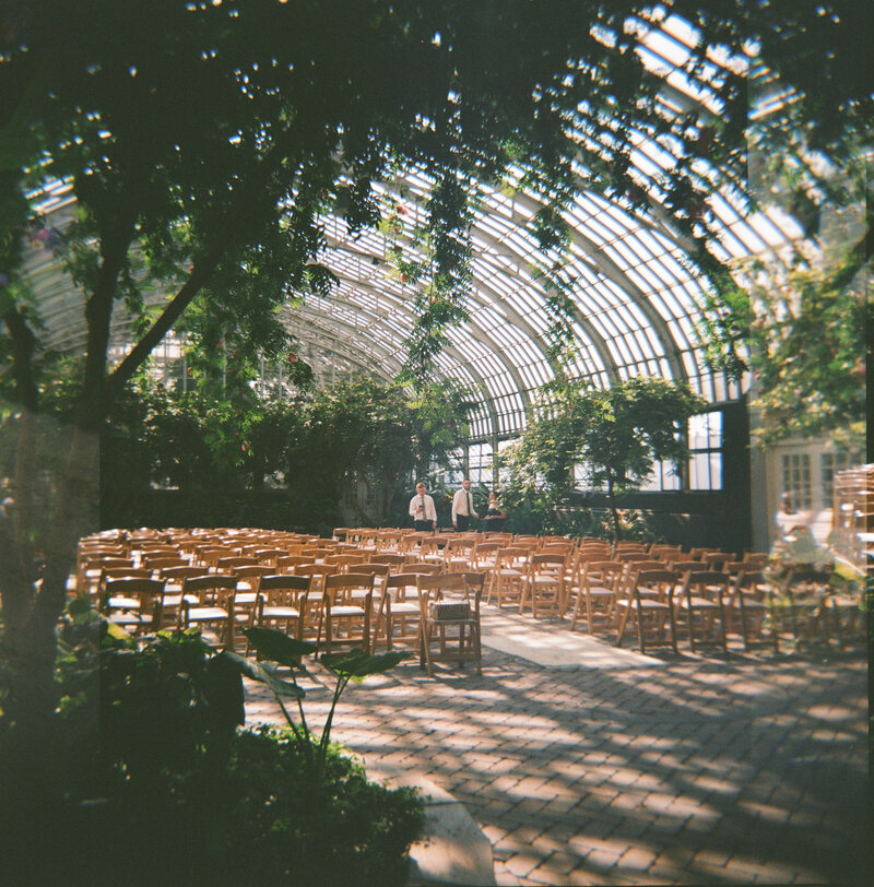 Setting up ceremony chairs in the bloom room at Garfield Park Conservatory, captured in a destination and documentary wedding style by Emily Ambie.