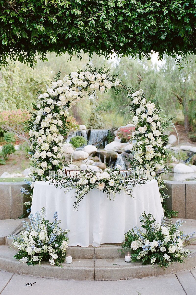 15-radiant-love-event-outdoor-ceremony-floral-whiterose-arch-behind-sweetheart-table-romantic-greenery-white-roses-romantic-elegant-timeless